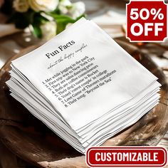 a stack of white napkins sitting on top of a wooden table next to a vase with flowers