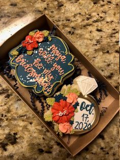 a decorated birthday cake in a box on a counter top next to a cookie that says happy new year