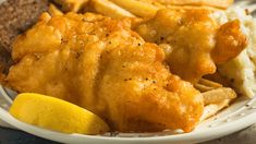 a white plate topped with fried fish next to french fries and lemon wedges on top of a table