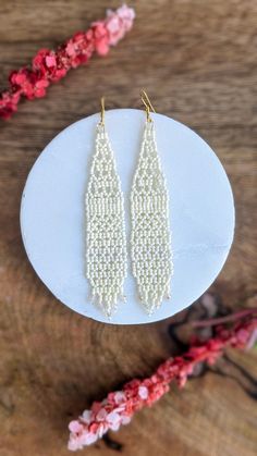 two white beaded earrings sitting on top of a wooden table next to pink flowers