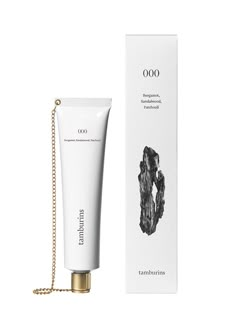 a tube of hand cream next to a white box and gold chain on a white background