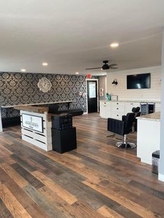 a large open kitchen and living room with wood flooring on the walls, white cabinets and black appliances