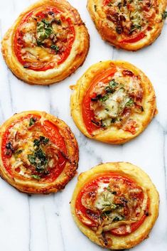 four small pizzas on top of a white marble counter with cheese and vegetables in the middle