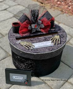 a black hat with skeleton hands and red bow on it next to a card box