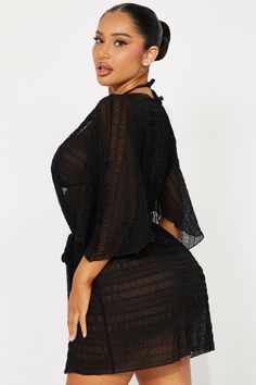 a woman wearing a black dress with sheer sleeves and an open back, posing for the camera