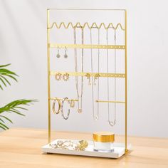 a gold jewelry rack with earrings and rings on it next to a potted plant