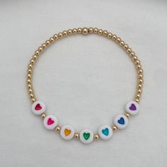 Add a colorful touch to your outfit with our Rainbow Hearts Bead Bracelet in luxurious gold fill. This playful accessory features a charming rainbow heart design that will surely bring a smile to your face. Perfect for any occasion, spread love and good vibes with this unique piece. Details: 3mm quality gold fill beads Accented with 7 7x4mm acrylic heart beads 14kt gold fill & sterling silver beads manufactured in the USA Beaded by hand on durable high performance elastic for a gentle stretch, m Hearts Bracelet, Gold Heart Bracelet, Rainbow Hearts, Gold Hearts, Rainbow Heart, Bead Stringing, Measuring Tape, Spread Love, Heart Beads