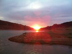 the sun is setting over a body of water with mountains in the backgroud