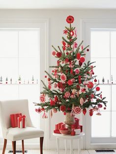 a christmas tree with red and white ornaments in a living room next to a chair