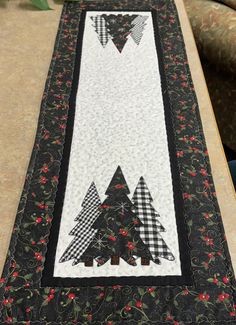 the table runner is decorated with black and white quilts, trees, and red berries