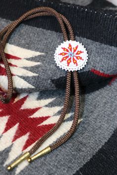 Stunning Native American beaded bolo tie with a burst pattern at the center.  This bolo tie is hand beaded and has the "mistake" beaded in to the piece showing that the bolo is not perfect which is a Native American custom and tradition.  This bolo has leather backing the bead work and is mounted on a brown woven cord with gold tone tips at the end of each cord.  This would make a fantastic addition to your bolo collection or to you Native American jewelry collection.  This piece has been worn and is being sold as is. Handmade Artisan Bolo Ties For Western-themed Events, Handmade Bohemian Bolo Tie, Bohemian Bolo Tie For Rodeo, Handmade Bohemian Bolo Tie For Rodeo, Handmade Festival Bolo Ties, Bohemian Lariat Bolo Tie For Rodeo, Handmade Southwestern Bolo Ties, Handmade Lariat Bolo Tie For Rodeo, Handmade Southwestern Lariat Bolo Tie