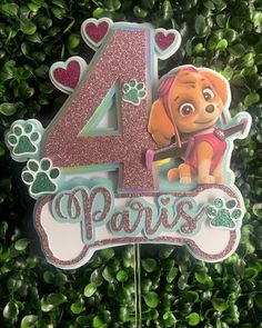 a birthday cake topper with the number four and paw patrol character on it in front of some green plants