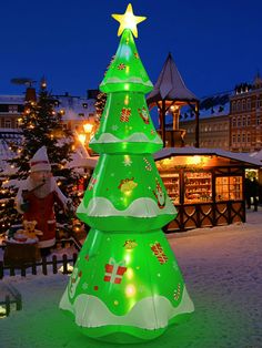 a lighted christmas tree in the middle of a snow covered ground with santa's and other holiday decorations around it