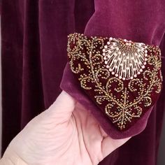 a hand holding a purple velvet purse with gold beading