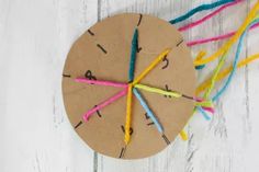 a clock made out of colored yarn on top of a white wooden table next to scissors