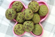 a pink heart shaped bowl filled with green chocolate chip muffins on top of a checkered table cloth