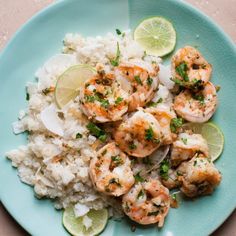 a blue plate topped with rice and shrimp next to lime wedges on top of it