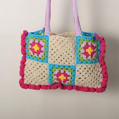 a crocheted bag hanging from a hook on a white wall with pink handles