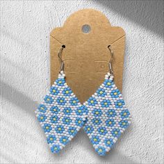 a pair of blue and white beaded earrings hanging from a hook on a wall