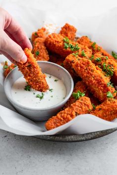 a person dipping some food into a bowl with ranch dressing on the side and another hand reaching for it