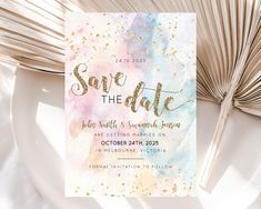 save the date card with watercolor paint and gold foil on it next to an open fan