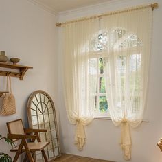 a living room with wooden floors and white curtains on the window sill, next to a round mirror