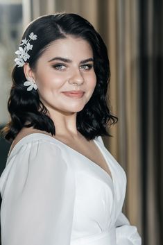 a woman in a white dress smiling and wearing a flower hair clip on her head