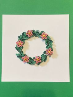 a paper wreath with pink and yellow flowers on it sitting on top of a piece of white paper