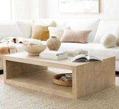 a living room with a white couch, coffee table and pillows on the floor in front of it