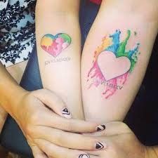 two women with matching tattoos on their arms holding onto each other's hands while they both have painted hearts