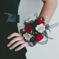 a woman wearing a black dress holding a red and white wrist corsage with flowers on it