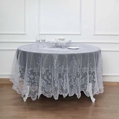 a round table with white lace on it in front of a wall and wooden floor