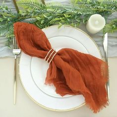 an orange scarf on a white plate with silverware and greenery in the background