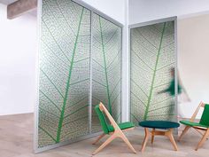 two green chairs sitting next to each other in front of a glass wall with leaves on it