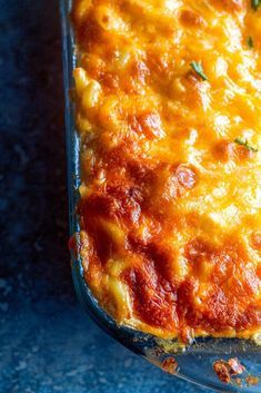 a casserole dish with cheese and meat in it sitting on a blue surface