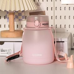 a pink blender sitting on top of a table next to a lamp and some other items