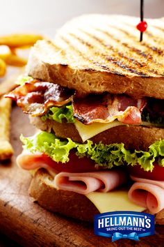 a bacon, lettuce and cheese sandwich on a cutting board with french fries