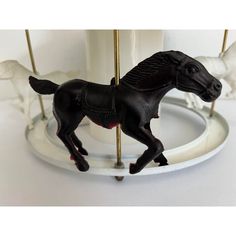 a black horse figurine sitting on top of a white carousel next to two white horses