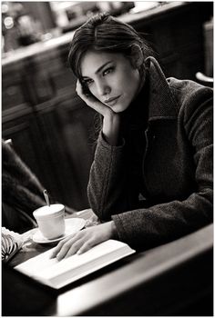 a woman sitting at a table in front of a book and coffee cup with her hand on her head