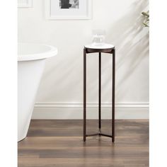 a small white table next to a bathtub in a room with wood flooring