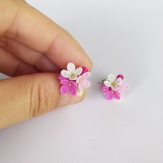 two tiny pink and white flowers are being held by someone's hand on a white surface