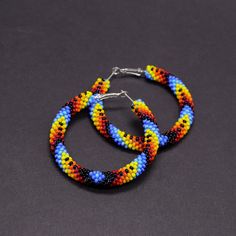 two pairs of multicolored beaded hoop earrings on a black surface with silver hooks