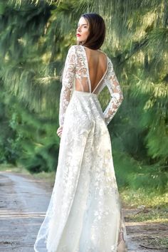 a woman in a white dress standing on a dirt road with her back to the camera