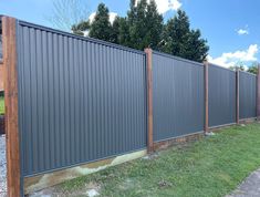 a large metal fence with wooden posts and grass in the foreground, next to a gravel path