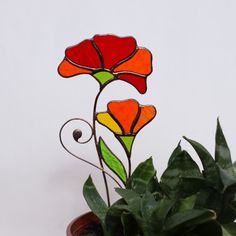 a stained glass flower sitting on top of a potted plant next to a white wall