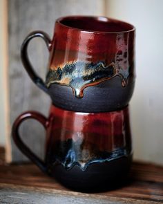 two red and black mugs sitting on top of a wooden table