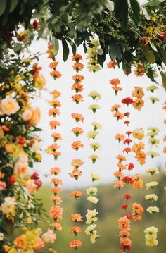 many flowers are hanging from the ceiling in front of a field with grass and trees