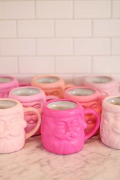 pink and white mugs with faces on them sitting on a marble counter in front of a brick wall