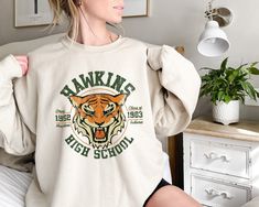 Hawkins High School Sweatshirt-Hoodie. Dear Buyer, Thank you for choosing us How to Order:  Choose your shirt color * Choose your size * Choose your design & text color * PLEASE make sure all your order's steps Color Disclaimer Prints may appear smaller depending on the shirt size ordered When will my product arrive? Processing Time: 1-3 days During holidays please expect delays as the amount of orders are slightly higher than usual, although we will do our best to get your order to you as soon Hawkins High School, Hawkins Indiana, Go Tigers, School Sweatshirts, Stranger Things 3, Tiger Shirt, Popular Shirt, Vintage School, Branded Sweatshirts