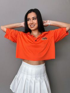 a woman in an orange shirt and white skirt posing for the camera with her hands on her head